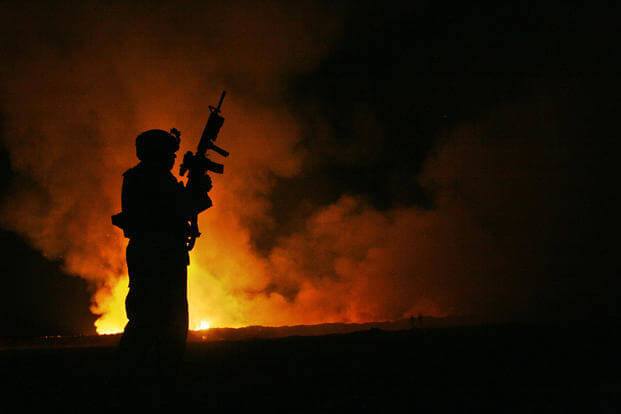 A Marine watches over a burn pit at Camp Fallujah, Iraq as smoke and flames rise into the night sky, May 25, 2007. (U.S. Marine Corps photo/Samuel D. Corum)