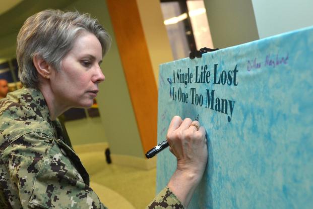 Lt. Cmdr. Karen Downer writes a name on a Suicide Awareness Memorial Canvas in honor of Suicide Awareness Month at Naval Hospital Jacksonville, Sept. 10, 2018. (U.S. Navy/Jacob Sippel, Naval Hospital Jacksonville).