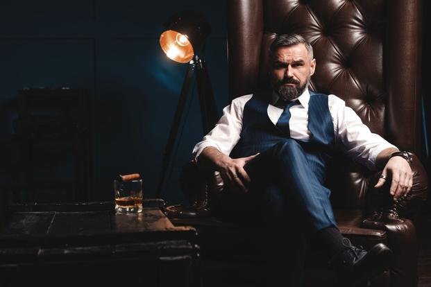 businessman in leather chair smokes cigar and drinks bourbon