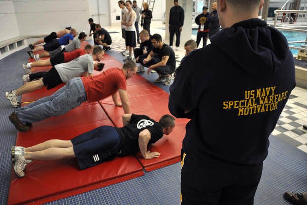 A special warfare special operations motivator monitors participants doing push-ups at a Navy SEAL Fitness Challenge at East Kentwood High School.