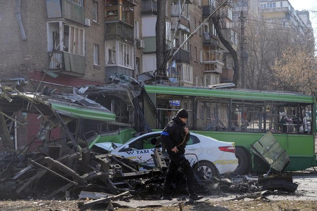 A Ukrainian soldier passes by a destroyed a trolleybus and taxi.