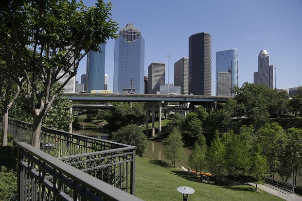 A railing from an apartment complex and the Houston skyline overlook the Buffalo Bayou as it snakes its way into downtown.