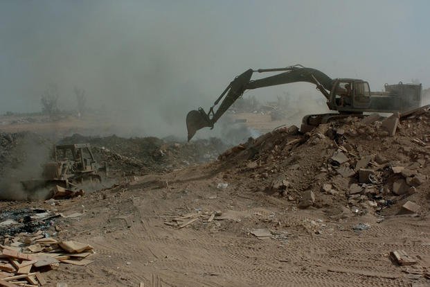 Soldiers use a bulldozer and excavator to maneuver trash and other burnable items around in a burn pit at a landfill in Balad, Iraq.