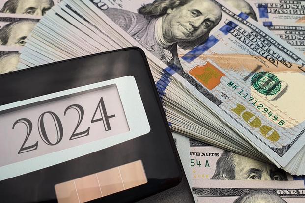 The year 2024 appears in a calculator display amid piles of $100 bills.