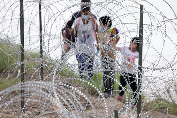 Migrants with children walk by razor wire fencing after crossing the Rio Grande River from Mexico into the U.S.