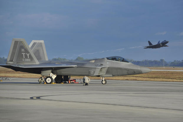 An F-22 Raptor from Tyndall Air Force Base, Fla., sits on the flightline while a Raptor launches from the Tyndall runway Dec. 10, 2015, during Checkered Flag 16-1. (Photo: Senior Airman Sergio A. Gamboa)