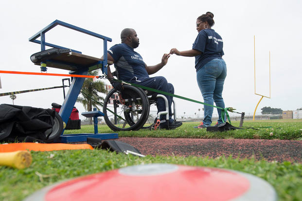 Shundra Johnson returns a wedding ring to her husband Coast Guard Lt. Sancho Johnson after his seated discus practice Navy’s wounded warrior training camp. Shundra is also her husband’s caregiver. (DoD News photo by EJ Hersom)