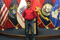 Raheel Siddiqui poses in front of U.S. military flags.