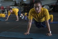 Sailors participate in group physical fitness training in the aircraft carrier USS Carl Vinson hangar bay.