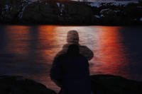 man is silhouetted against lights reflected in the waters off Cape Neddick in Maine