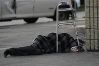 A person sleeps under a light rain on a sidewalk in Los Angeles.