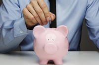 Businessman drops coin in pink piggy bank.