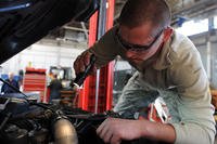 Service member repairing auto engine with a flashlight.